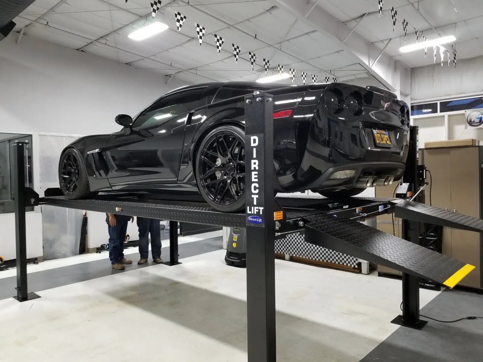Gallery Black Corvette C6 Z06 on a Direct Lift PP8S four-post lift with rear ramps extended in an indoor automotive shop