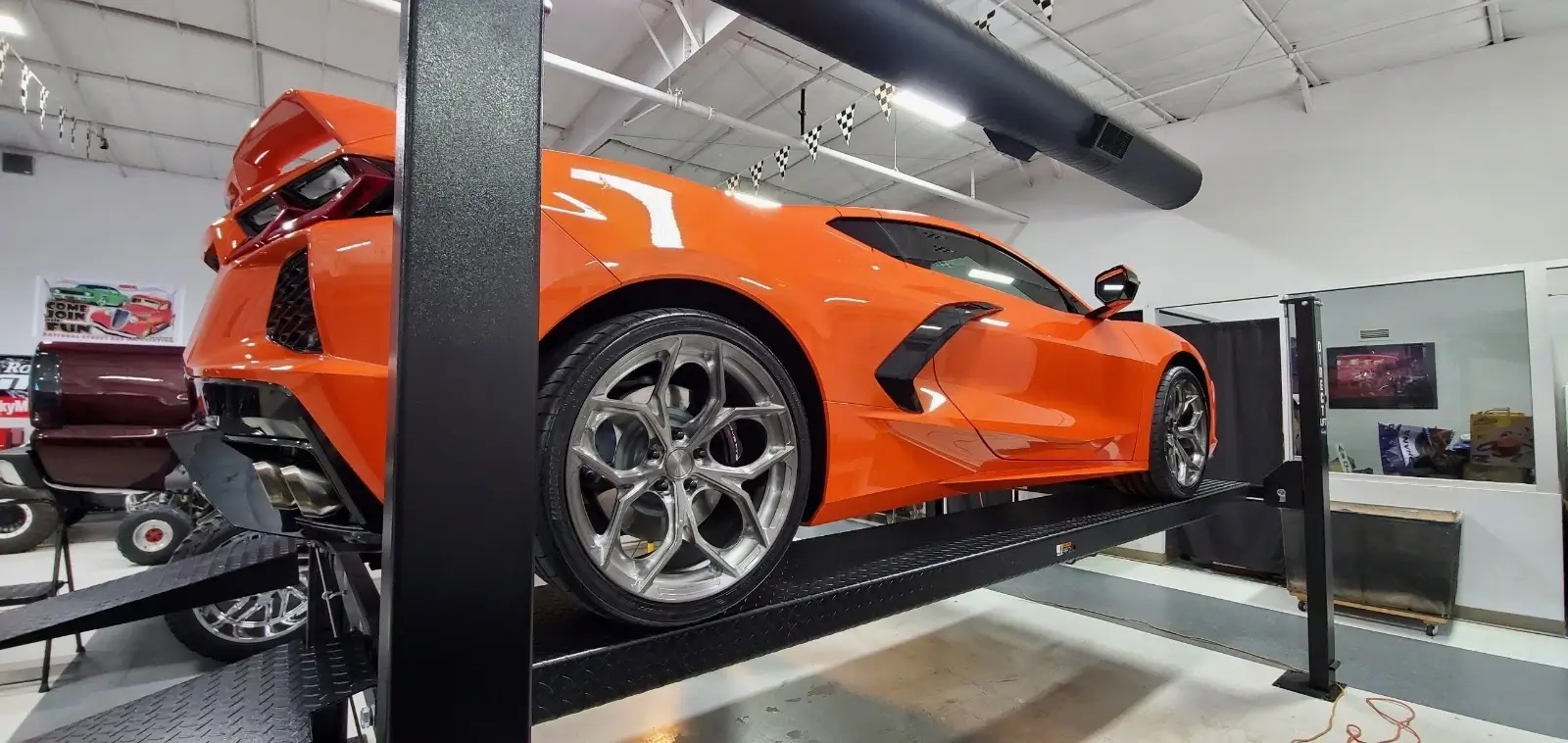 Gallery Bright orange C8 Corvette elevated on a Direct Lift PP8S four-post automotive lift in a modern showroom
